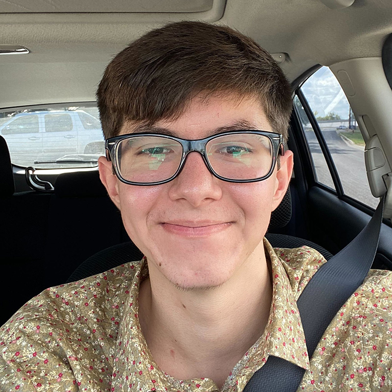 Levi Long sits in a car wearing a patterned shirt and glasses.